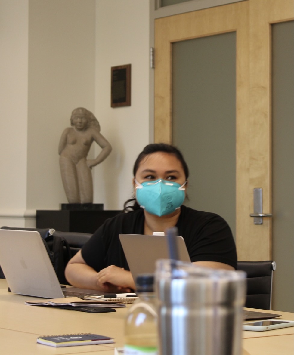 Dr. Ashley Caranto Morford is seated at a desk covered in notebooks, laptops, and other materials.